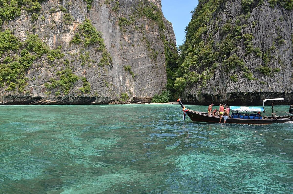 Boat crossing turquoise water between limestone cliffs in Thailand
